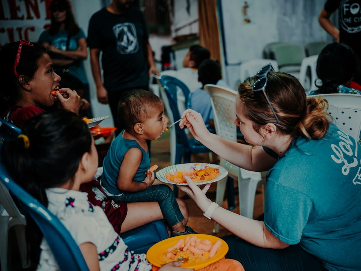A caregiver offers a plate of food to a young child during a meal.